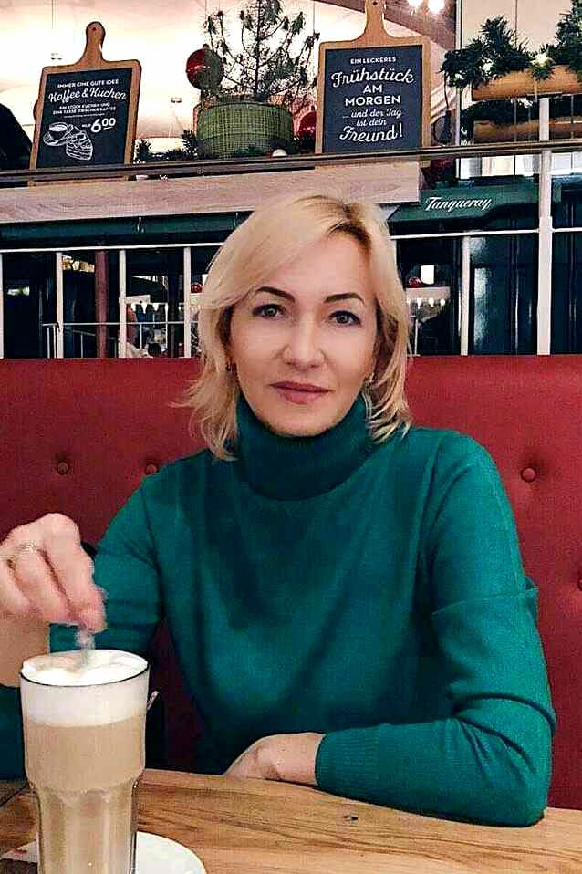 Blonde Frau in einem grünem Pullover trinkt Cappuccino.